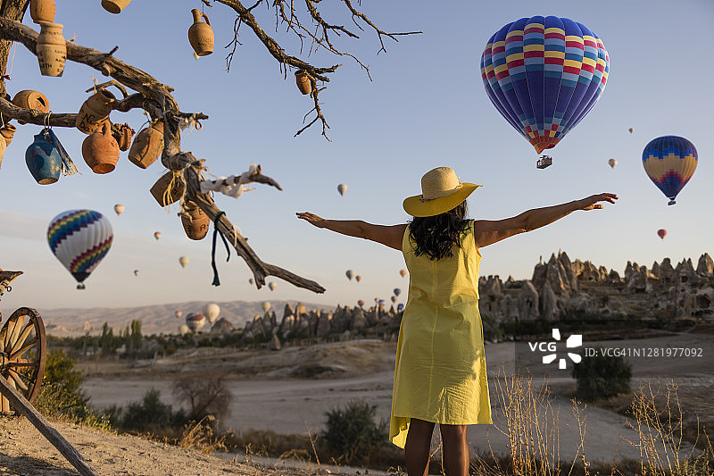 在土耳其卡帕多西亚，美丽的女人看着彩色的热气球飞过山谷。图片素材
