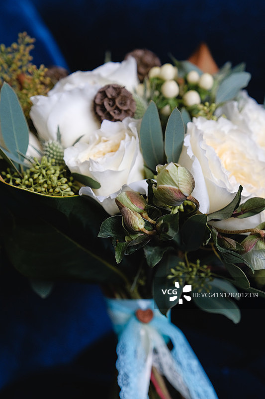漂亮的婚礼花束放在豪华的丝绒椅子上，特写。不同的花束和绿叶，用缎带系着，背景模糊。婚礼的主题。图片素材