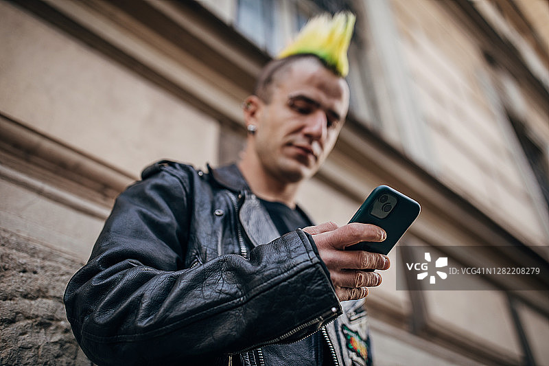 一个梳着五颜六色发型的年轻人在街上用智能手机拍照图片素材