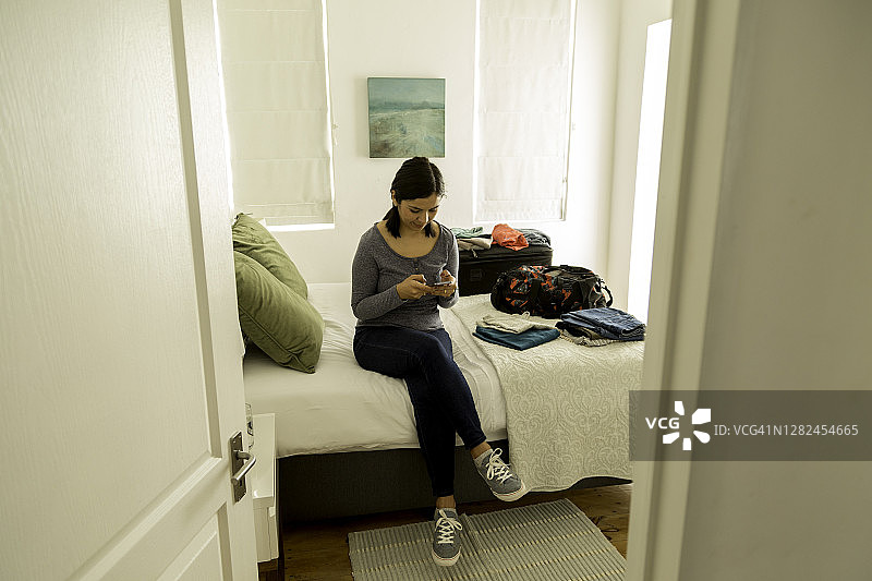 一个女人在公寓的卧室里看智能手机图片素材