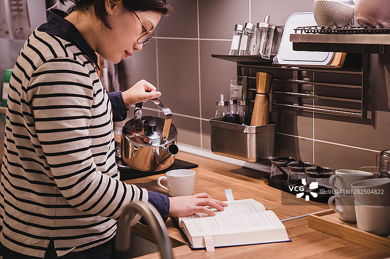 亚洲女性在家学习——在厨房柜台上阅读教科书图片素材