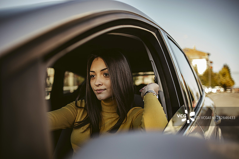 年轻的学生自豪地坐在她的新车-快乐的司机驾驶一辆车-一个快乐的专注的司机在路上开车的女人的肖像图片素材