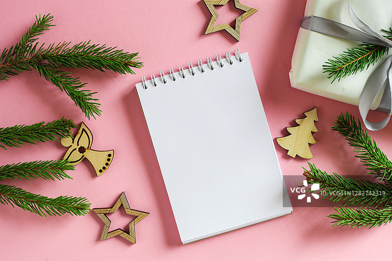 空白空白页的笔记本与复制空间。圣诞节天然松树或冷杉树枝粉红色的背景。圣诞彩灯，松果和植物天然装饰。图片素材