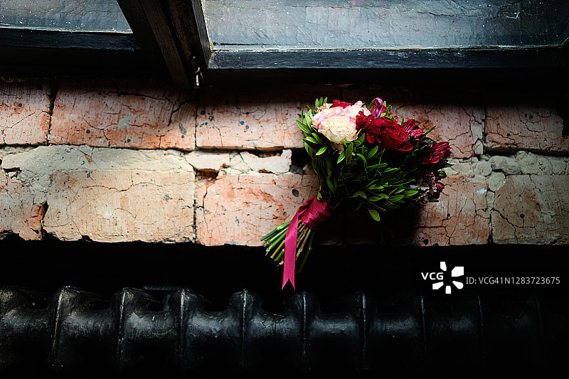 美丽的婚礼花束在一个破旧的旧砖窗台和一个木窗的背景，特写。一束不同的鲜花和绿叶用缎带绑着，背景模糊。婚礼的主题。图片素材