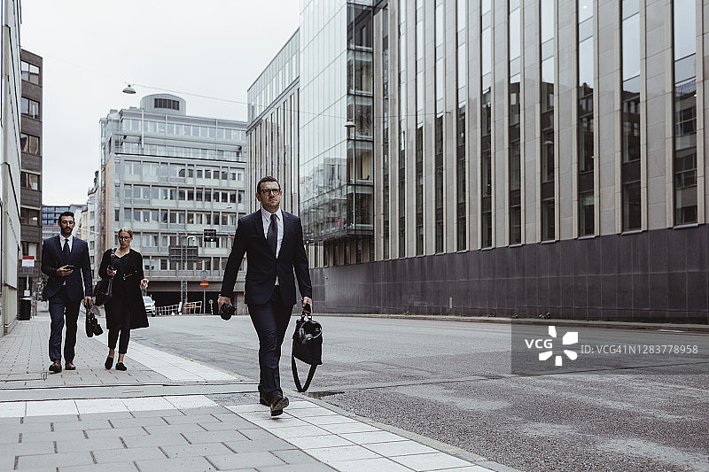在城市里，拎着包走在同事前面的男企业家图片素材