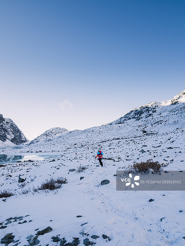 登山者在寒冷的雪地里徒步行走，沿着部分结冰的高山湖泊的海岸图片素材