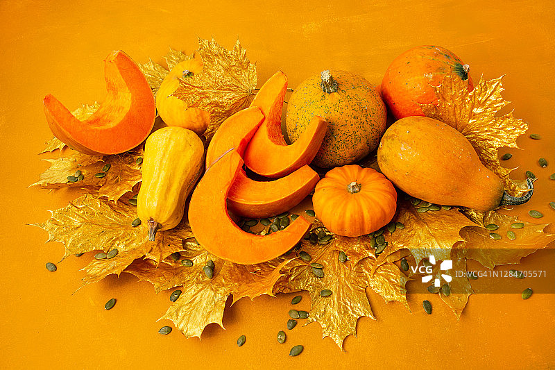 在橙色的背景上用南瓜和树叶装饰秋天的节日装饰。平铺秋的构图与临摹空间。图片素材