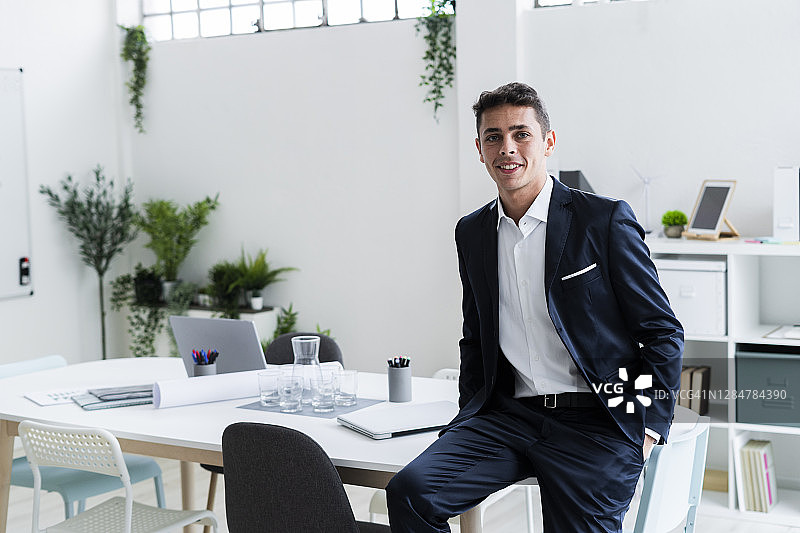 微笑的男性企业家坐在创造性的工作场所的办公桌上图片素材