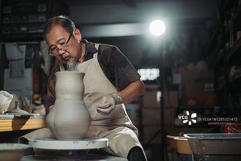 亚洲华人高级陶艺师在他的工艺工作室里，在一个旋转的陶轮上制作陶器图片素材