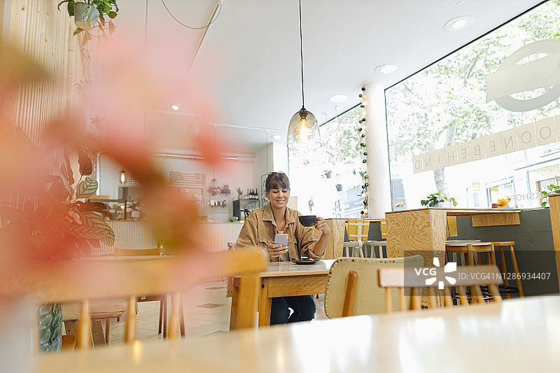女企业家拿着咖啡杯坐在咖啡馆里用智能手机发短信图片素材