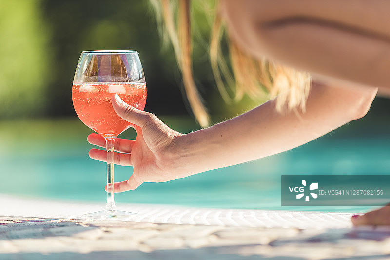 在意大利伦巴第曼托瓦的豪华泳池边，一名年轻女子拿着一杯鸡尾酒图片素材