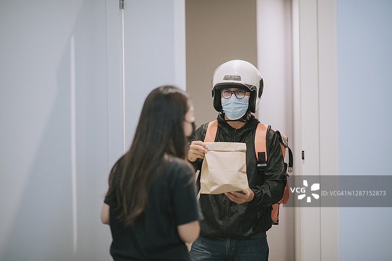 戴着头盔和外科口罩的亚裔华人送货员按门铃送食品图片素材