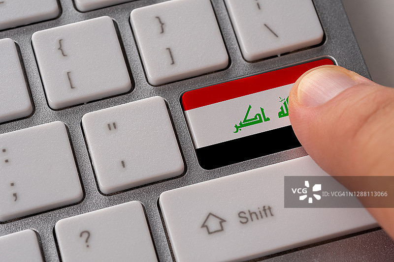 男性的手按键盘上的伊拉克国旗按钮。网上国际经营理念。图片素材