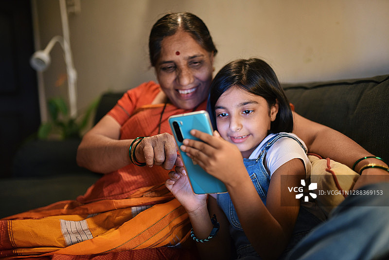 奶奶和孙女坐在沙发上玩智能手机图片素材