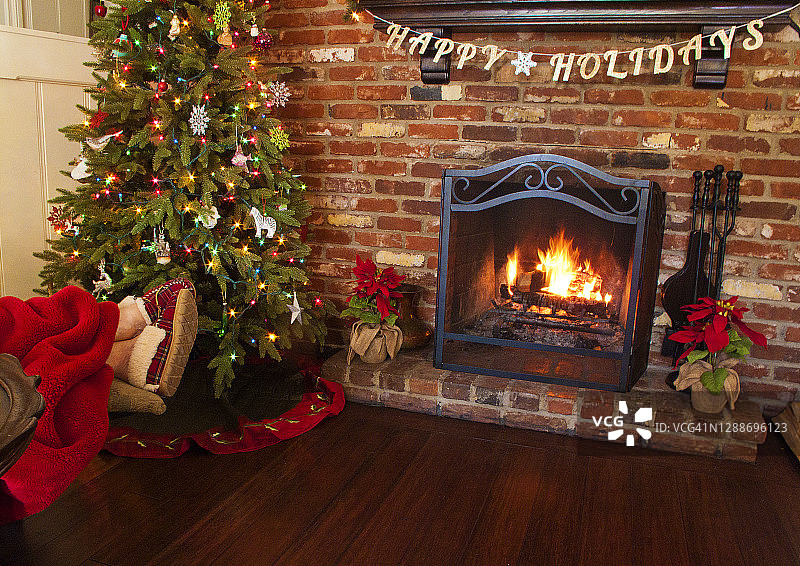 一个穿着舒适拖鞋的女人的脚，在圣诞树旁，在熊熊燃烧的壁炉前图片素材