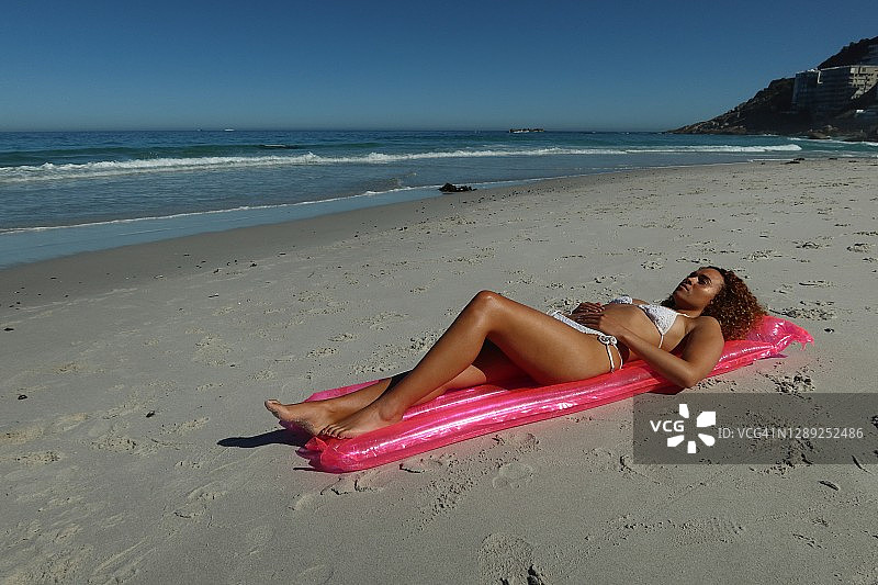 一个年轻漂亮的女人懒洋洋地躺在沙滩上一个粉红色的充气气球上图片素材
