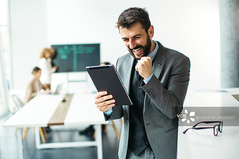 微笑的年轻商人看着平板电脑在现代化的办公室图片素材