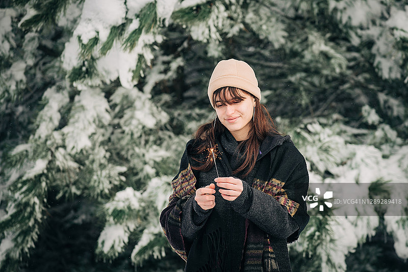 在白雪覆盖的圣诞树前，一个梦想的女孩手里拿着一个闪闪发光的东西图片素材