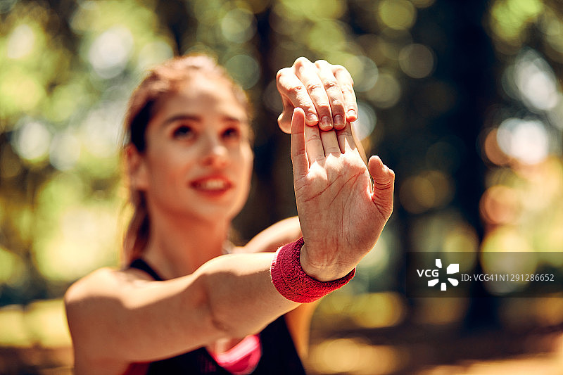 年轻的健康微笑女性跑步者的形状伸展她的手和做热身运动之前，在大自然中跑步。选择性的专注于手。图片素材