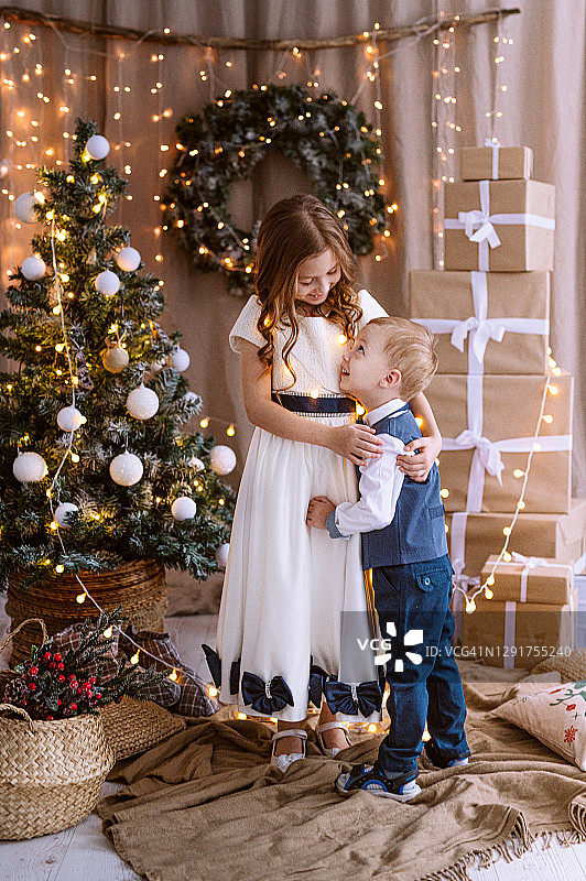 两个欧洲孩子在圣诞树下打开礼物盒，庆祝传统的圣诞节和新年图片素材