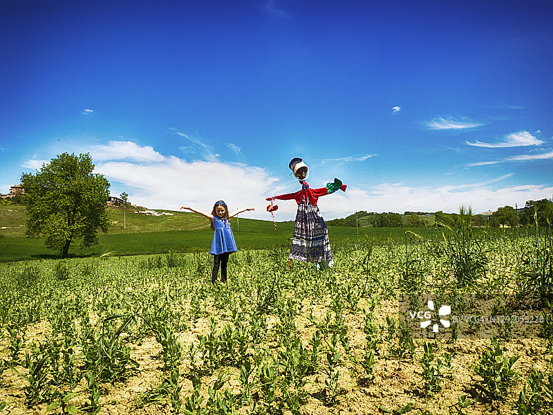 意大利，一个女孩站在一个稻草人旁边，双臂张开图片素材