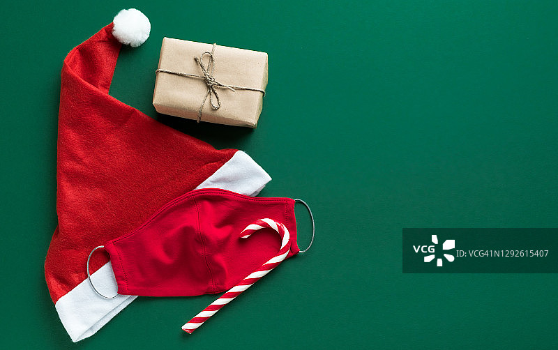 防护红色医用口罩，圣诞老人帽或帽，条纹糖果，礼物用黄麻绳系，在绿色背景上。预防和预防COVID - 19大流行的传播。快乐健康圣诞的理念。图片素材