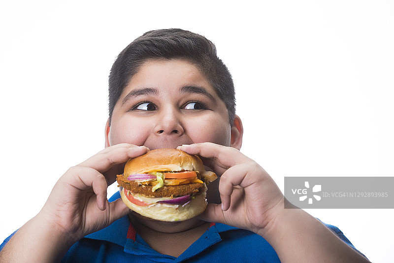 小男孩饥饿地吃着手里的一个汉堡。(肥胖)图片素材