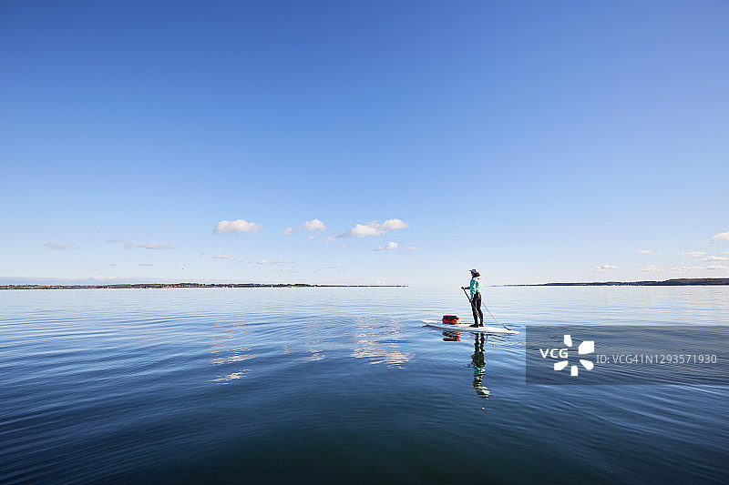 妇女在海上划桨，蓝天倒映在平静的水面上图片素材