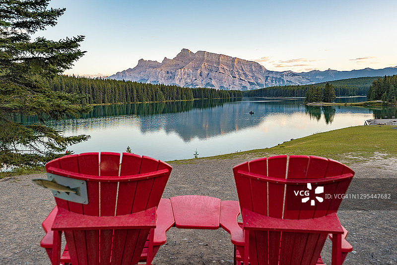加拿大日落时的两张杰克湖和伦德尔山的倒影，前景是两张红色的椅子图片素材