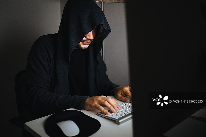 一名穿着连帽衬衫和面具的男子在黑暗中使用笔记本电脑黑客图片素材