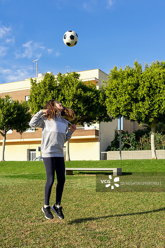 一个美丽的小女孩在一个美丽的公园里踢足球，在一个阳光明媚的冬天图片素材