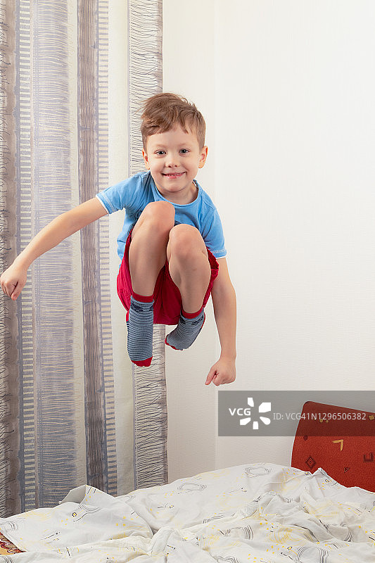 穿着蓝色t恤和红色短裤的小男孩在床上跳得很高图片素材
