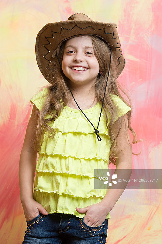孩子，小女孩微笑着戴着牛仔帽在彩色的背景图片素材
