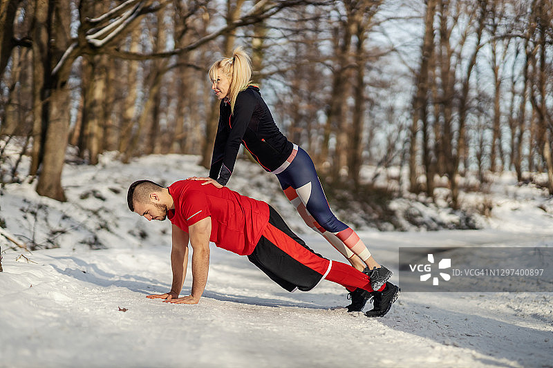 运动员在冬天做俯卧撑，而女运动员站在他的背后。关系，冬季健身，健康生活图片素材