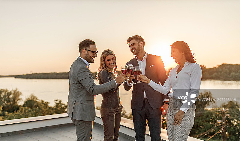 快乐的企业家们在阳台上用红酒敬酒。图片素材