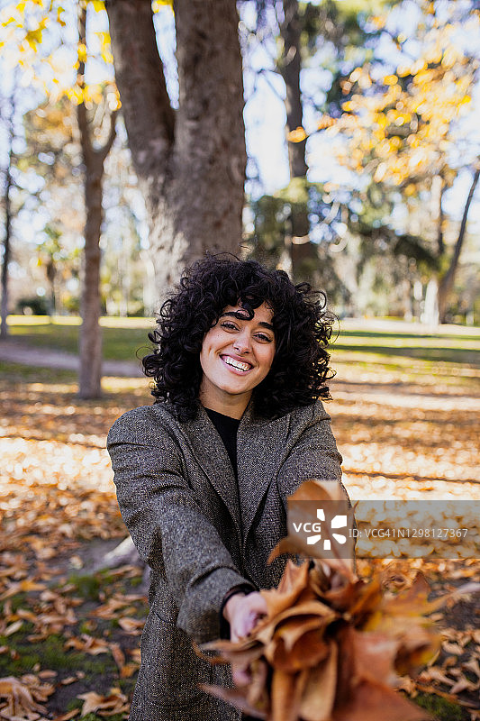 微笑的女人拿着干树叶站在公园里图片素材