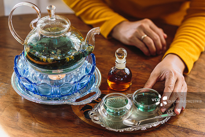 茶道概念，妇女坐在玻璃茶壶和茶杯前，在家里的木桌上放着糖浆瓶图片素材
