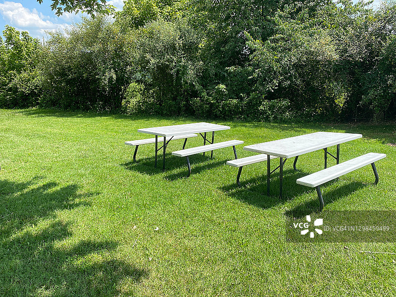 两张白色的野餐桌在一个郁郁葱葱的绿色花园区域，草坪和林地树木图片素材