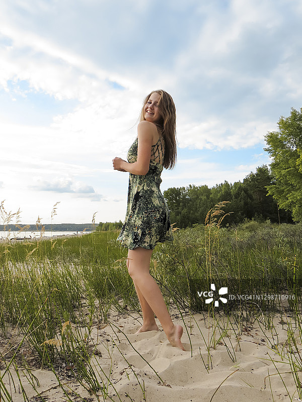 美丽的年轻的金发女人在一个炎热的夏天在一个沙滩上的一个短的夏天的海滩上以绿色的森林和多云的天空为背景图片素材
