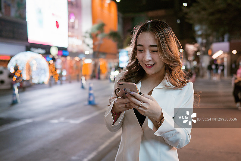 年轻的女商人晚上在市中心用智能手机图片素材