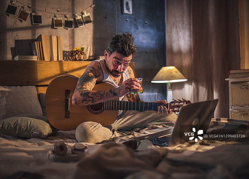 有纹身的嬉皮士坐在床上弹原声吉他，图片素材