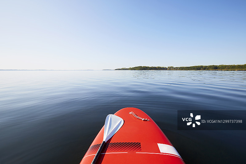 从一个红色的SUP桨板看平静的大海，蓝色的天空倒映在水中图片素材