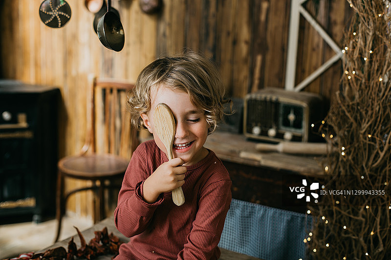 一个用木勺遮住一只眼睛的男孩在一个老式厨房里图片素材