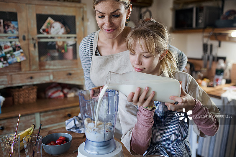 母亲和小女儿在室内厨房里，准备奶昔饮料。图片素材