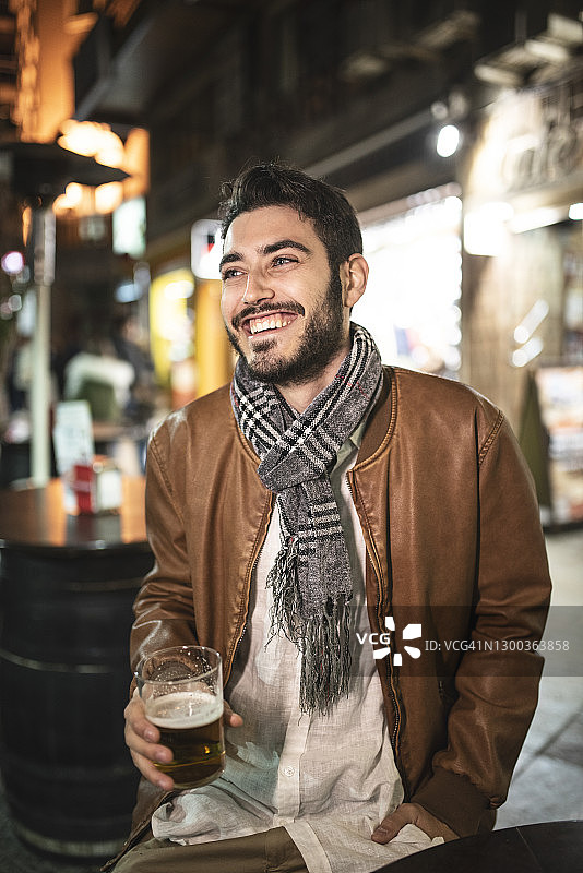 一个年轻人在酒吧的露台上喝啤酒。笑着喝酒开心图片素材