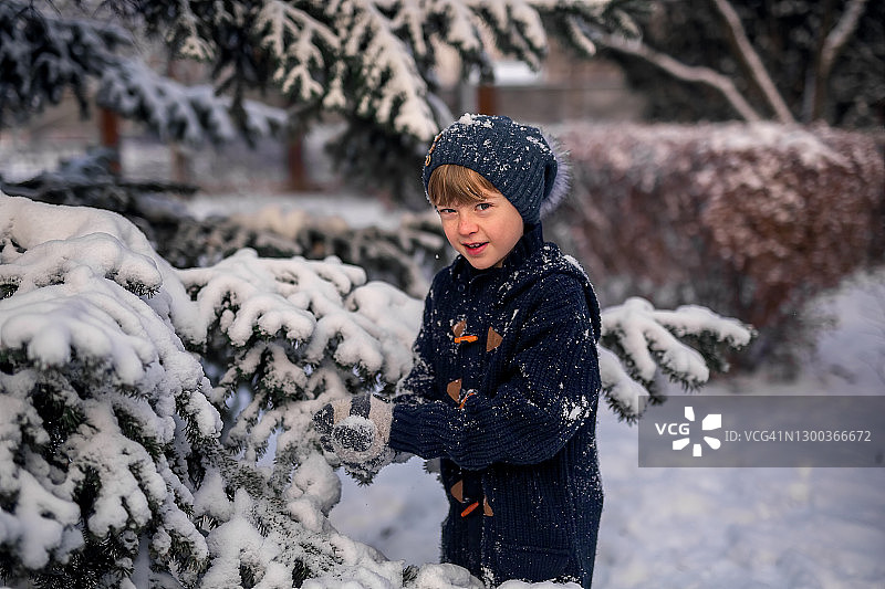 冬天。雪。一个男孩在街上的雪树旁玩耍。图片素材
