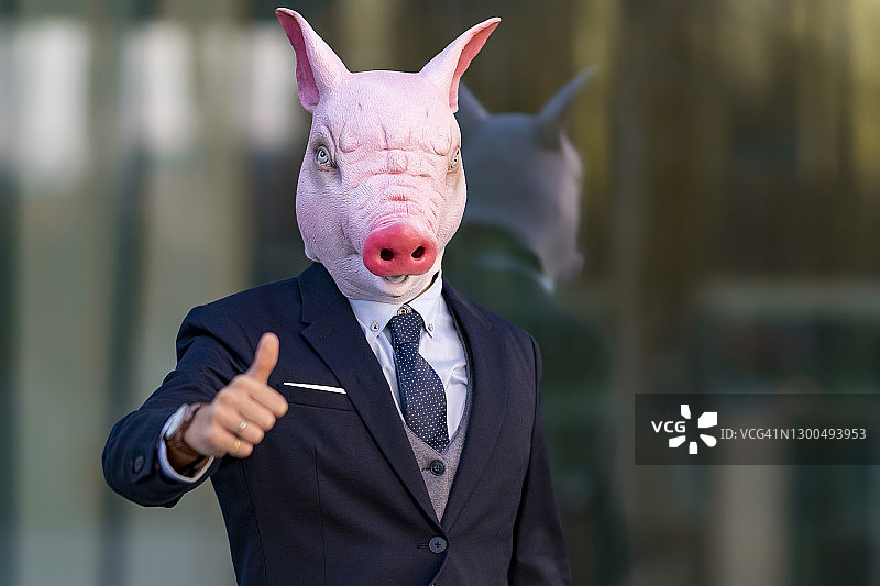 年轻商人戴着猪面具对着办公楼竖起大拇指图片素材
