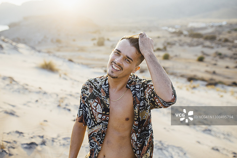西班牙塔伯纳斯阿尔梅里亚的沙漠中，一名手握头发的快乐年轻人图片素材
