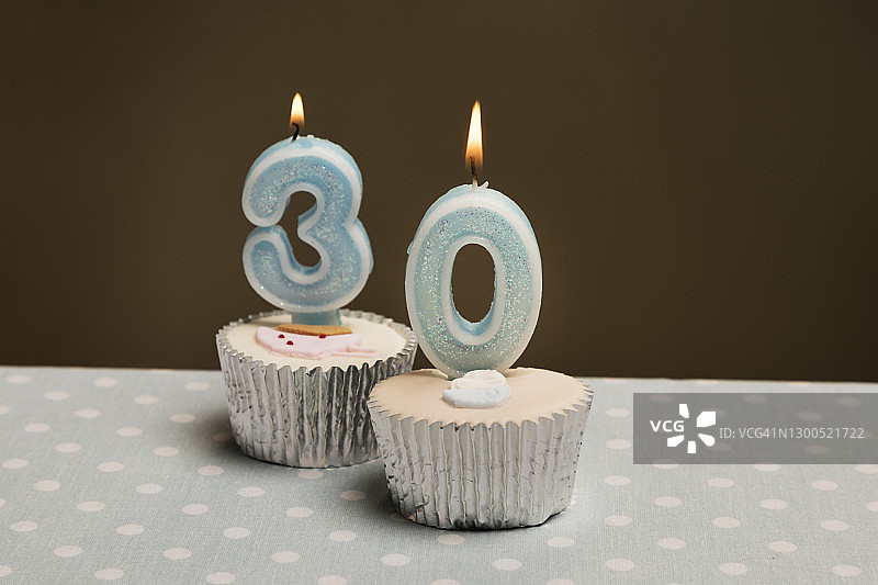 工作室拍摄的纸杯蛋糕上面点着蜡烛，上面写着数字30。图片素材