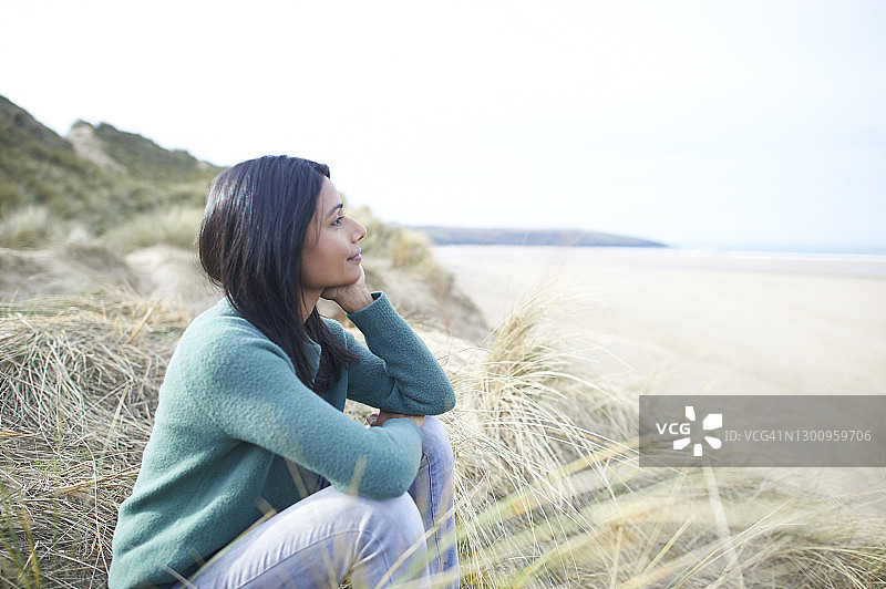 美丽安详的亚洲女人坐在海滩上眺望大海。图片素材